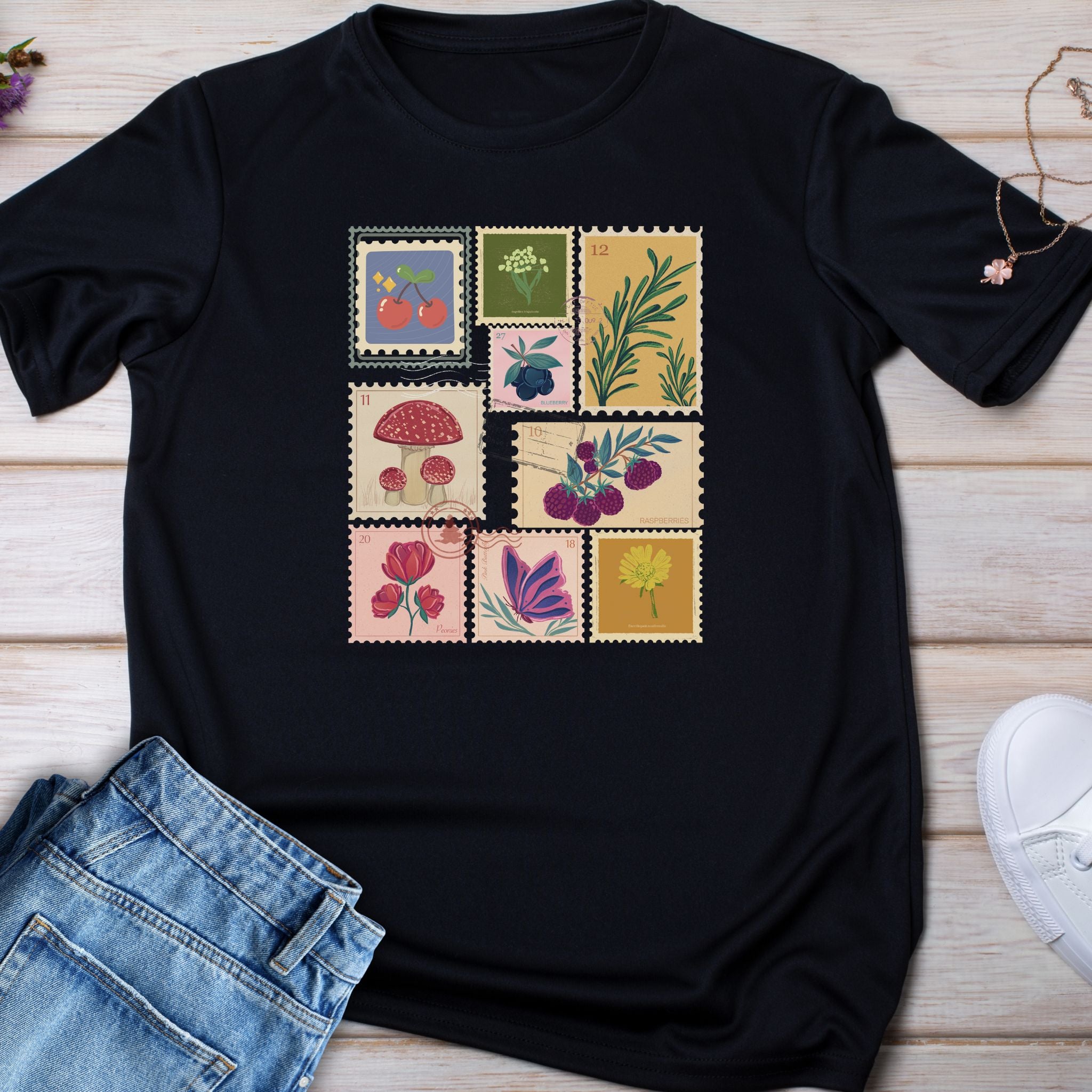 Black t-shirt with colorful stamp-like design on a wooden surface with jeans and sneakers.